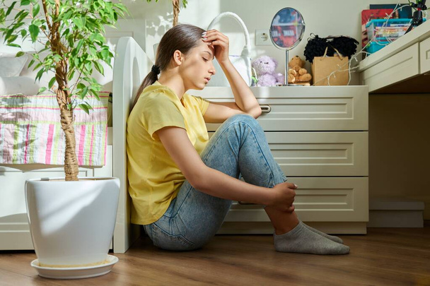 Sad teenage girl sitting on the floor at home. Upset female high school student in room. Teenage problems, stress, depression, adolescence, mental health concept - Photo, image