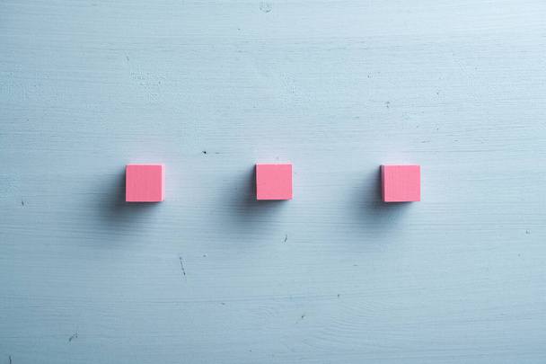 Tres bloques de madera rosa en blanco colocados sobre fondo de madera azul pastel. - Foto, imagen