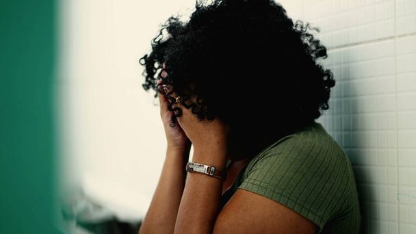 Одна испуганная молодая черная женщина, сидящая на полу, покрывая лицо стыдом. Испуганная афро-американская бразильская девушка страдает от одиночества - Фото, изображение