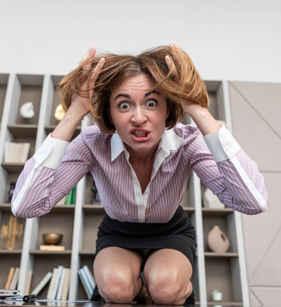 Angry female office worker standing on the table and demonstrating her irritation and dissatisfaction of work - Foto, Bild