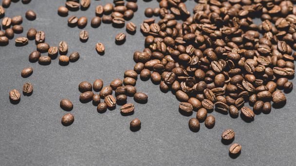 Des grains de café uniformément éparpillés sur un fond noir, des grains de café aromatiques bruns rôtis. - Photo, image