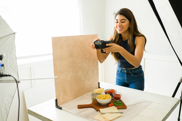 Vidám ételfotós a stúdióban mosolyogva, miközben a professzionális fényképezőgépével fényképez  - Fotó, kép