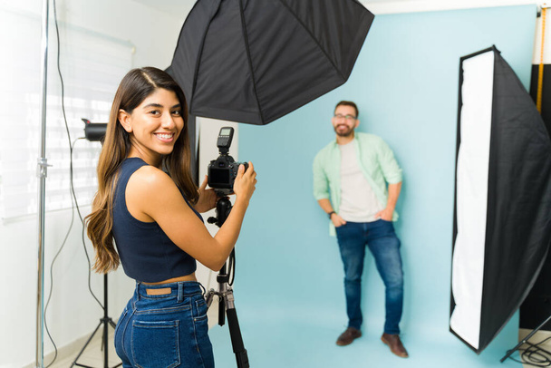 Wesoła kobieta fotograf uśmiecha się nawiązując kontakt wzrokowy podczas pracy z modelką podczas sesji zdjęciowej - Zdjęcie, obraz