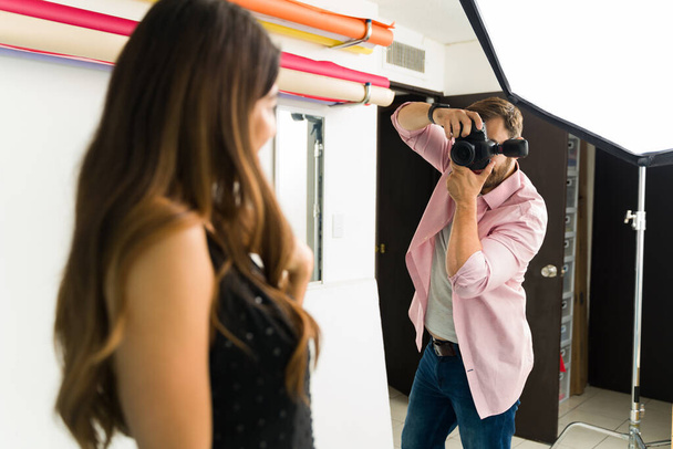 Photographe caucasien prenant des photos avec un appareil photo professionnel et travaillant avec un mannequin femme au studio - Photo, image