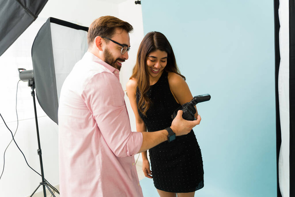 Happy photographer and latin model laughing while checking the professional photos on the camera after a photo shoot - Photo, Image