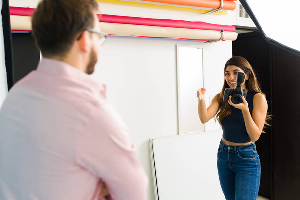 Mujer feliz fotógrafa hablando con un modelo masculino durante una sesión de fotos en su estudio profesional - Foto, imagen