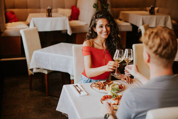 Mooi jong koppel lunchen met witte wijn in het restaurant - Foto, afbeelding