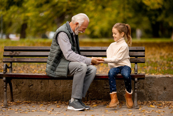Hermoso abuelo jugando manos rojas juego de bofetadas con su nieta en el parque en el día de otoño - Foto, Imagen