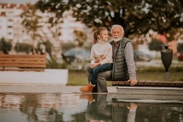 Jóképű nagyapa ősszel az unokájával tölti az idejét egy kis medencénél a parkban. - Fotó, kép