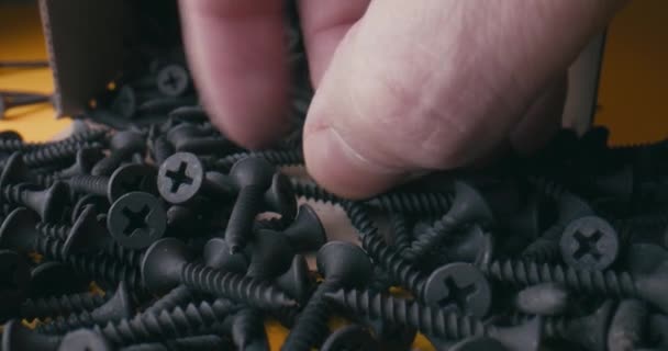 Hand picking screws that fall out of the box on an yellow background. Super macro close up slow motion view of black screws. - Footage, Video