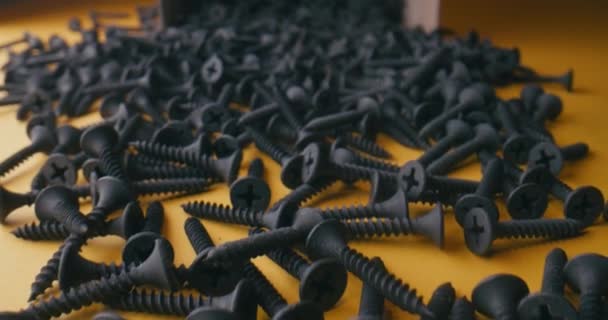 Hand picking black screws that fall out of the box on an orange background. Super macro close up black screws slow motion view. - Footage, Video