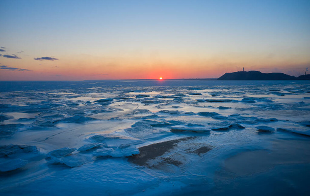 Aerial view of sunset over the frozen sea. Winter landscape on seashore during dusk. View from above of melting ice in ocean on sunrise with a horizon. Global warming. Vivid colorful skyline scenics. - Valokuva, kuva