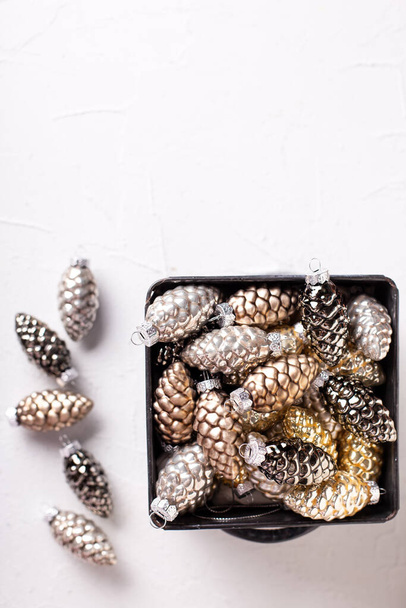 Christmas decorations. Metallic box with glass gold, black, silver decorative cones on white  textured background. Scandinavian minimalistic style. Still life. Place for text. - Photo, Image