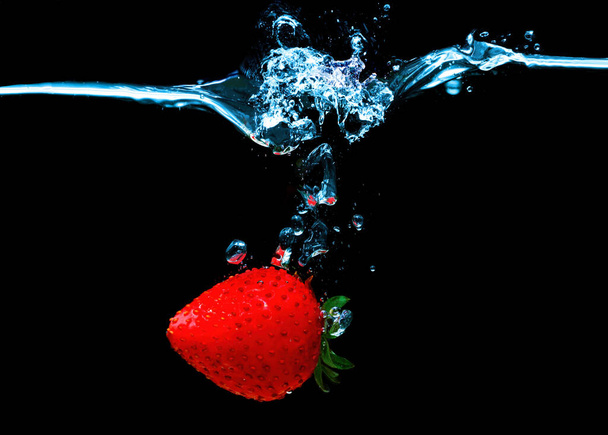 Single whole ripe strawberry sinking underwater with splashes isolated on black background. - Fotoğraf, Görsel