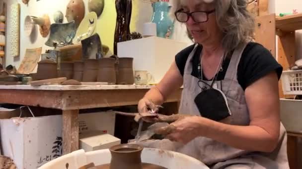 Een vrouw meet de grootte van een deksel voor een stuk aardewerk dat ze meteen maakt. Ze heeft het op de tafel laten drogen. Nu maakt ze een afgewerkt product voor de keuken - Video