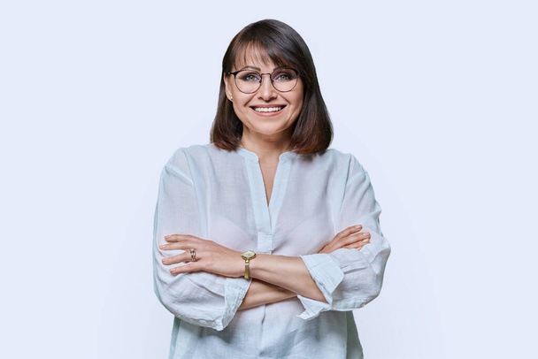 Attractive middle aged woman looking at camera on white background. Smiling confident 40s female with glasses, crossed arms in white shirt. Lifestyle confidence calmness mature people concept - Zdjęcie, obraz