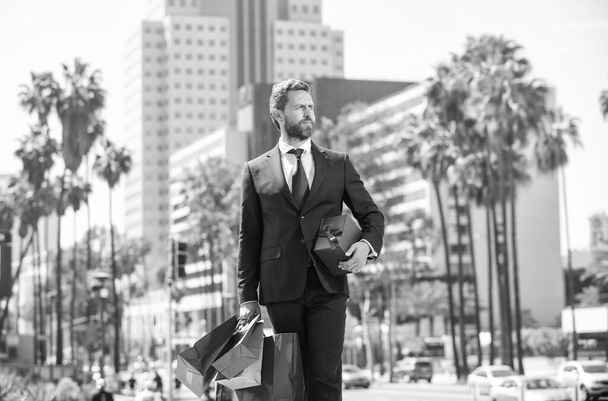 bärtiger Geschäftsmann in Formalbekleidung spaziert mit Einkaufstüten vor das Büro, Jubiläum. - Foto, Bild