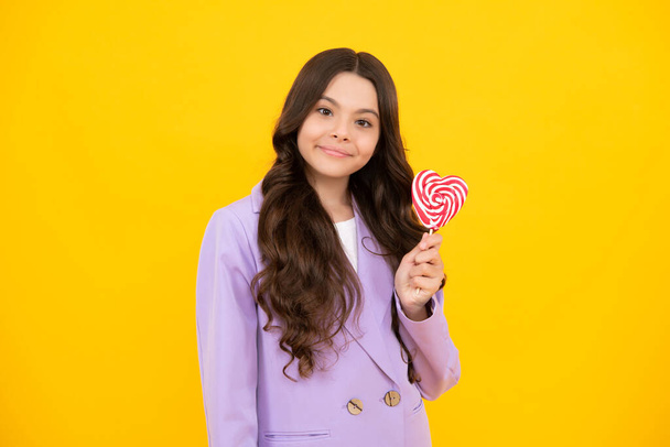 Happy teenager, positive and smiling emotions of teenager girl with lollypop. Candy and sweets for kids. Child eat lollipop popsicle over yellow isolated background. Yummy caramel, candy shop - Foto, Bild