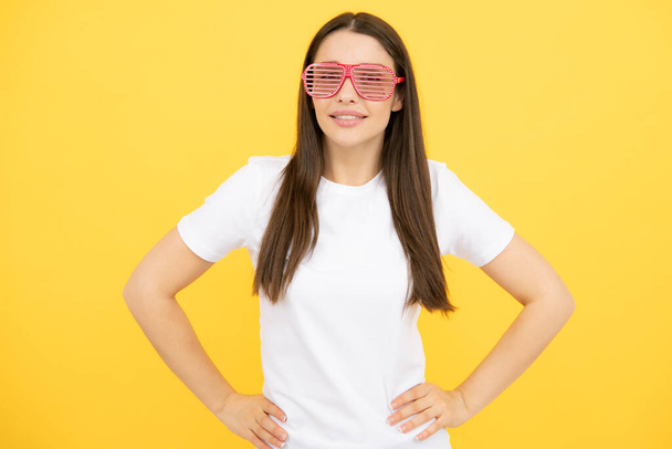 Χαρούμενο κορίτσι με μεγάλα αστεία γυαλιά ηλίου για πάρτι. Πορτρέτο της νεαρής γυναίκας φορώντας αστεία γυαλιά απομονώνονται σε κίτρινο φόντο - Φωτογραφία, εικόνα