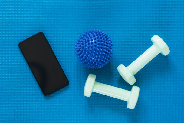 ボールやダンベルとスポーツマット上の黒い画面で現代のスマートフォンのトップビュー。フラットレイアウト、モックアップ。オンライントレーニングコンセプト. - 写真・画像