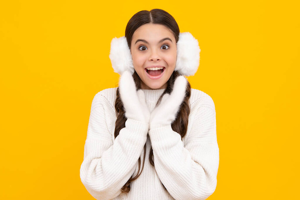 Tinédzser lány téli meleg fülvédővel fülvédővel izolált sárga háttér felett. Téli karácsonyi ünnepek, újévi hangulat. A gyerekek meleg ruhát. Izgatott tinédzser lány - Fotó, kép