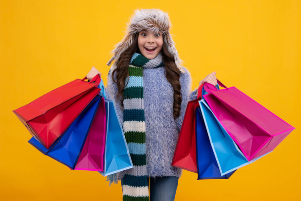 Kışın sıcak şapka takan ergen bir kız çocuğu alışveriş çantasında kış indiriminin tadını çıkarıyor. Sonbahar alışverişi. Çocuk kız alışverişe gitmeye hazır. Heyecanlı genç kız - Fotoğraf, Görsel