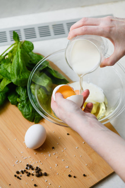 Žena rozbije vejce do skleněné misky a nalije mléko, aby udělala omeletu.. - Fotografie, Obrázek