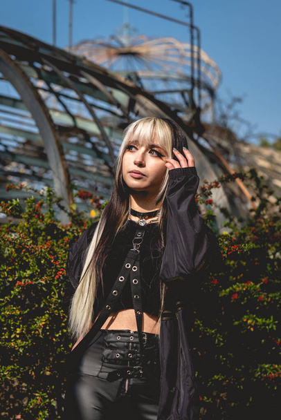 Young and skinny model with long blonde and black hair and black clothes and makeup posing inside an old abandoned greenhouse - Foto, Bild