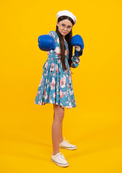 Young child girl using boxing gloves with funny face. Portrait of funny surprised winner teenage girl in boxing gloves isolated on yellow - Φωτογραφία, εικόνα