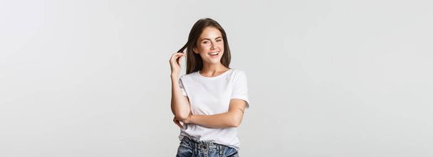 Portrait of sassy attractive young woman, playing with hair strand and smiling satisfied. - Foto, Imagen