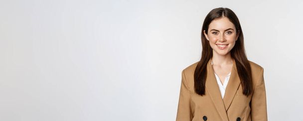Portret van een zakenvrouw met enthousiaste gezichtsuitdrukking, glimlachend, zelfverzekerd, staand in pak over een witte achtergrond. - Foto, afbeelding