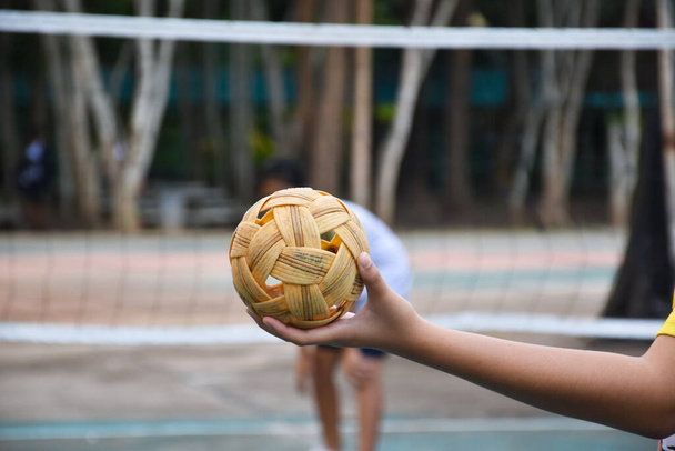 Sepak takraw ball, southeast asian countries traditional sport, holding in hand of young asian female sepak takraw player in front of the net before throwing it to another player to kick over the net. - Photo, Image