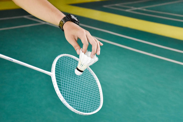 El jugador de bádminton sostiene la raqueta y el volante de crema blanca frente a la red antes de servirlo en otro lado de la cancha. - Foto, Imagen
