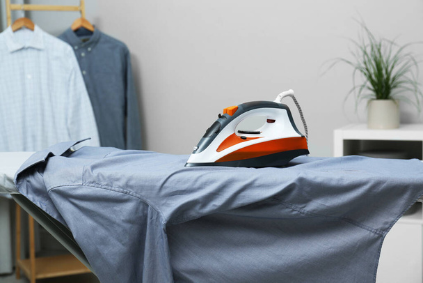Modern iron and grey shirt on board indoors - Фото, изображение