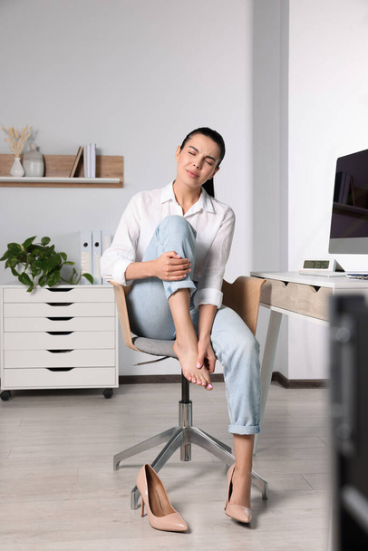 Young woman rubbing sore foot in office - Foto, afbeelding