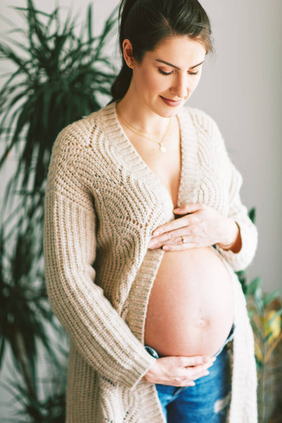 幸せな若いです妊娠中の女性の屋内肖像暖かいニットジャケットを着て - 写真・画像