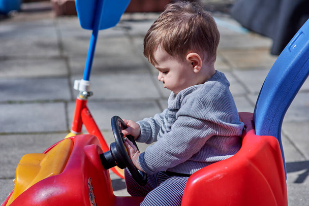 hermoso joven niño está jugando en un rojo empuje coche - Foto, imagen