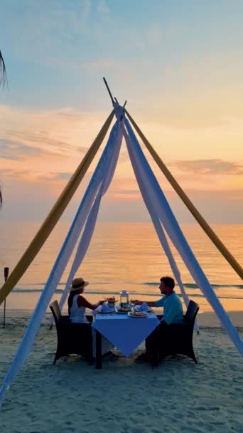 Dîner romantique sur la plage avec de la nourriture thaïlandaise pendant le coucher du soleil sur l'île de Koh Chang Thaïlande. Un couple d'hommes caucasiens et de femmes thaïlandaises asiatiques ayant un dîner romantique sur la plage - Séquence, vidéo