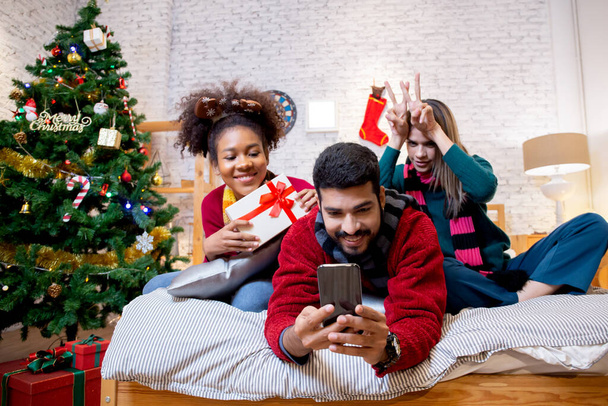 家で一緒にスマートフォンで興奮して楽しんでいる若い友人をグループ化します。,男性と女性は陽気でお祝いのクリスマスの前夜に写真を撮る, xママと新年や休日の概念. - 写真・画像