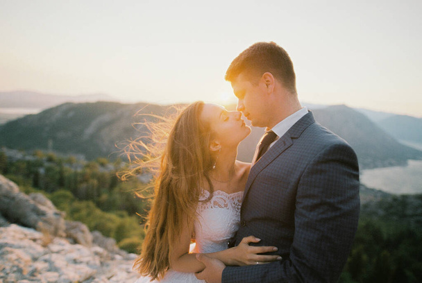 Bride almost kisses groom high in the mountains in the rays of the setting sun. High quality photo - Photo, Image