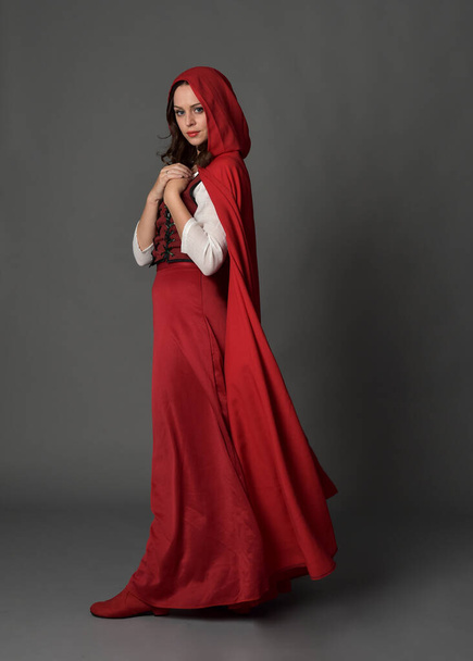 長いスカートと流れるフード付きクロークと赤い中世のファンタジーの衣装を身に着けている美しいブルネットの女性の完全な長さの肖像画。. - 写真・画像