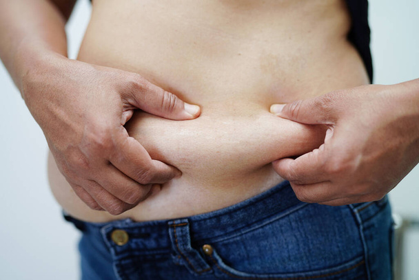 太りすぎアジアの女性は脂肪腹を圧迫するために手を使用します大きなサイズ太りすぎと肥満. - 写真・画像