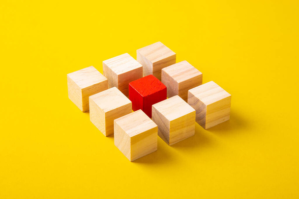 Czerwony drewniany blok wyróżniający się z grupy drewniane klocki na żółtym tle. - Zdjęcie, obraz