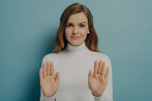 Αυτοπεποίθηση νεαρή γυναίκα δείχνει τις παλάμες της, ενώ κρατώντας και τα δύο χέρια απλωμένα σε στάση χειρονομία απομονωμένη πάνω από το μπλε φόντο τοίχο στούντιο, Καυκάσιος θηλυκό λέει όχι. Έννοια της άρνησης - Φωτογραφία, εικόνα