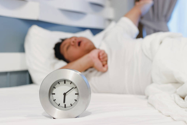 Alarm clock waking up at morning with a man sleeping on bed. - Φωτογραφία, εικόνα