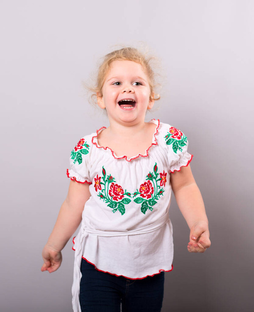 A sweet little round-faced girl in a smart embroided shirt on grey background. Studio shot - Foto, Imagem