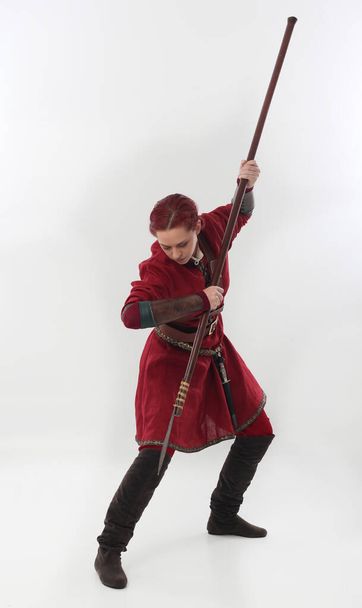 volledig portret van een mooie vrouw in een rood middeleeuws fantasie krijger kostuum met lederen harnas, met wapens. Staande houding geïsoleerd op witte studio achtergrond. - Foto, afbeelding