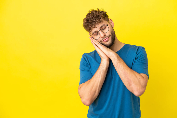 Young handsome caucasian man isolated on yellow background making sleep gesture in dorable expression - Fotó, kép