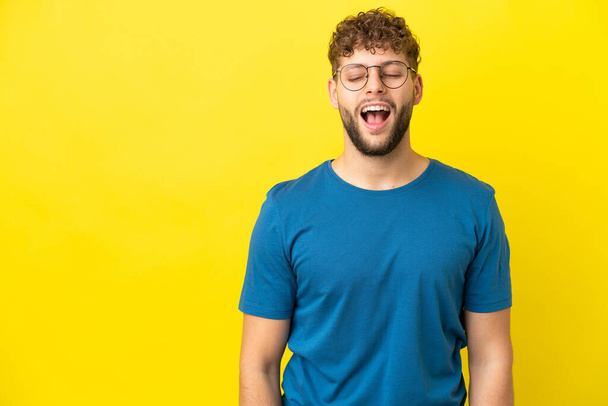 Young handsome caucasian man isolated on yellow background shouting to the front with mouth wide open - Foto, afbeelding