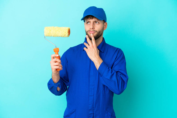 Painter caucasian man isolated on blue background having doubts while looking up - Foto, Imagem